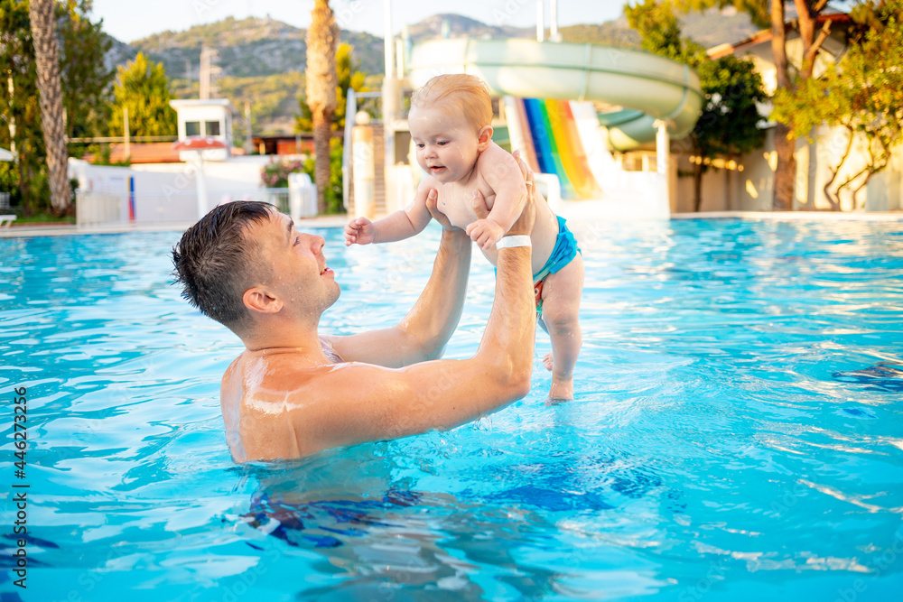 dad and baby in the pool with water slides in the summer have fun swimming, relaxing and spending time with the family on vacation, throwing the child up