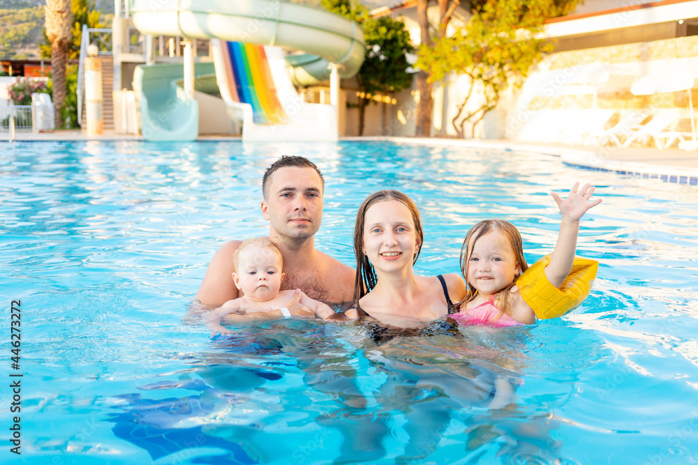 Fototapeta premium happy family mom, dad and two children are swimming in the pool with water slides and having fun on vacation, smiling and laughing