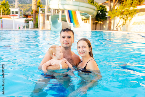 happy family mom, dad and baby daughter are swimming in the pool with water slides and having fun on vacation