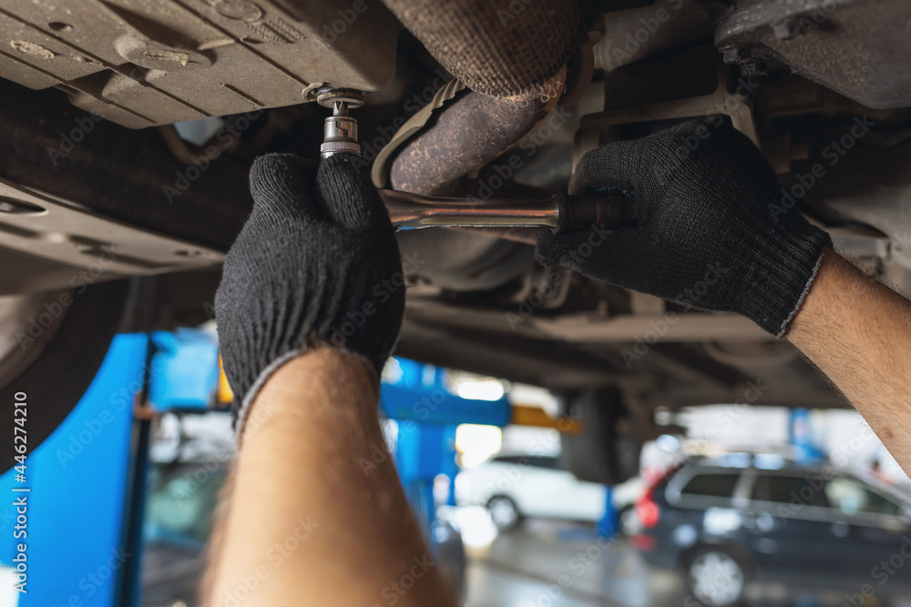 Obraz premium An auto mechanic unscrews the oil drain plug in the cars crankcase with a key, close-up