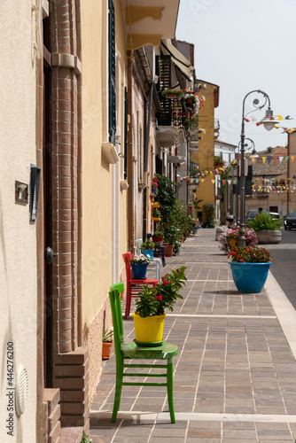 June 2021, San Vito Chietino, Italy. Main square of San Vito Chietino, old colored chairs next to the entrance doors of the houses, for tired travelers and to support flower pots. © silvia
