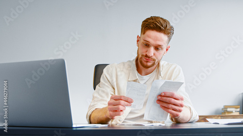 Bearded financial director analyzes paper checks searching for money waste and unexpected expenses at table