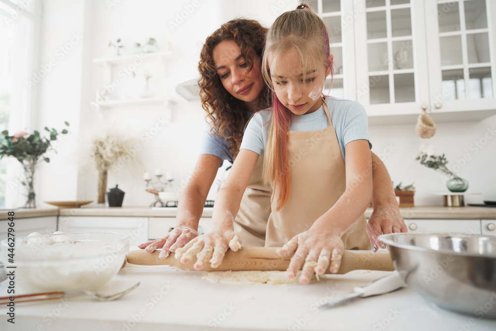 Teen girl helping her mom to cook dough in their kitchen at home Teen girl helping her mom to cook dough in their kitchen at home
