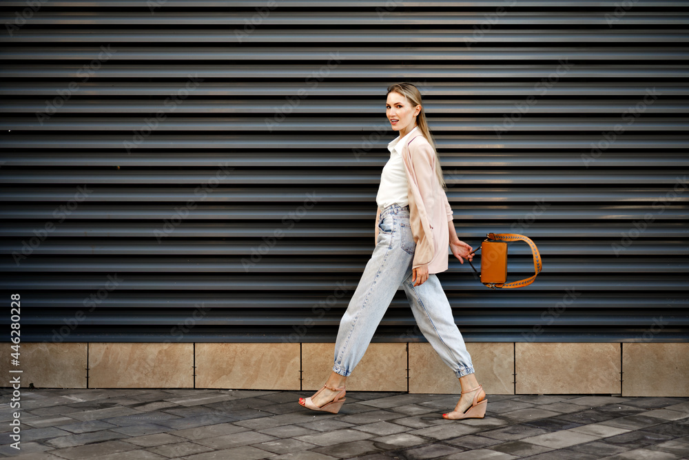 Fototapeta premium Stylish young businesswoman walking on the city street on sunny day