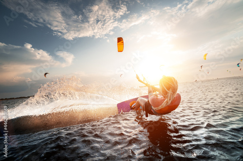 Professional kite surfer woman rides on a board with a plank in her hands on a leman lake with sea water at sunset. Water splashes and sun glare. Water sports photo