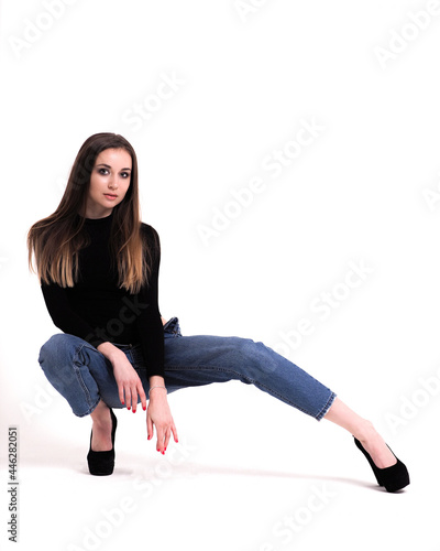 Brunette on a white background in a bodysuit and jeans with heels and with a ponytail