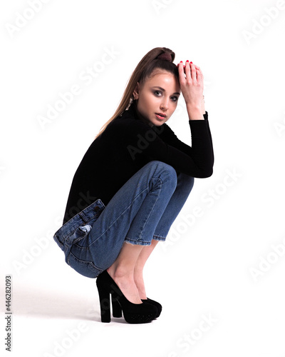 Brunette on a white background in a bodysuit and jeans with heels and with a ponytail