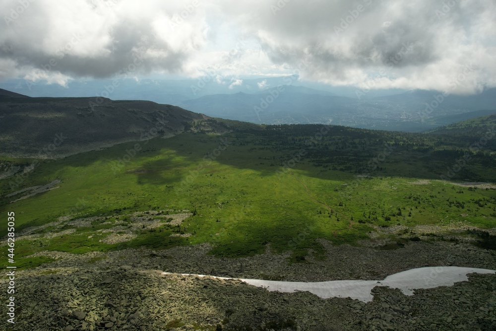 Fototapeta premium a mystical panorama of a mountain valley in July with the remnants of fresh snow. high in the mountains with a beautiful morning sky on the background. tourism and travel