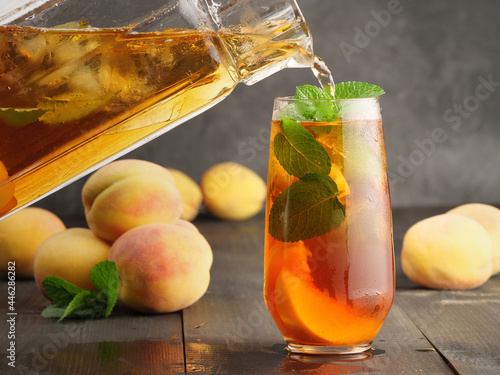 Peach ice tea with mint and ice on a dark wooden background.