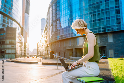Blonde business woman wearing glasses sit with laptop among the skyscrapers and work © Olga