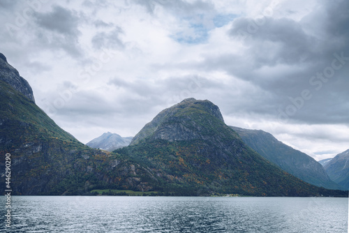 Majestic mountains tower above lake in northern Norway on a cloudy day of Arctic summer. Small houses between the mountains far in the distance. Mysterious Norwegian landscape. © Petr