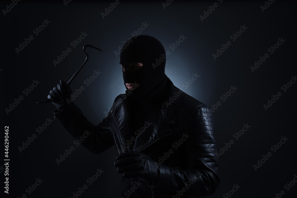 Man wearing knitted balaclava with crowbar on black background