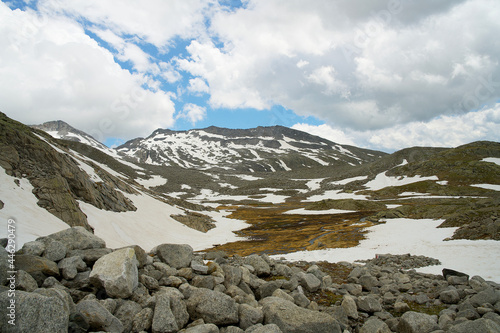 high alpine landscape with rocks, snowfields and blue sky with clouds