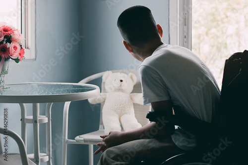 Disabled child on wheelchair talking with a white teddy bear on chair in blue room, Lifestyle of disability kid home alone the best friend is toy, Sad emotional and depression concept, Cinematic Tone. photo