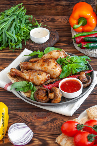 Grilled chicken on a wooden board, with hot pepper, vegetables and sauce, with juicy basil and tarragon on a brown wooden background