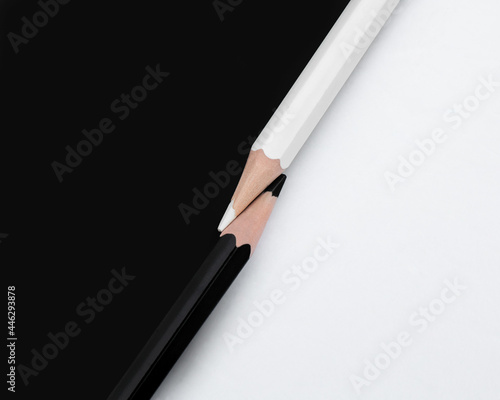 Macro shot of two black and white colored pencils with the tips touching on a matching background with opposite colors. Top down view flat lay. Concept of contrast or opposites attract