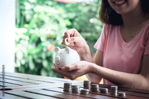 People put coins into the piggy bank, On wood table with blur background, concept to Saving money for investment and retirement age.