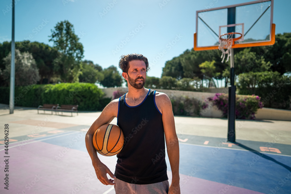 Handsome tired basketball player standing on basketball court outdoors in summer