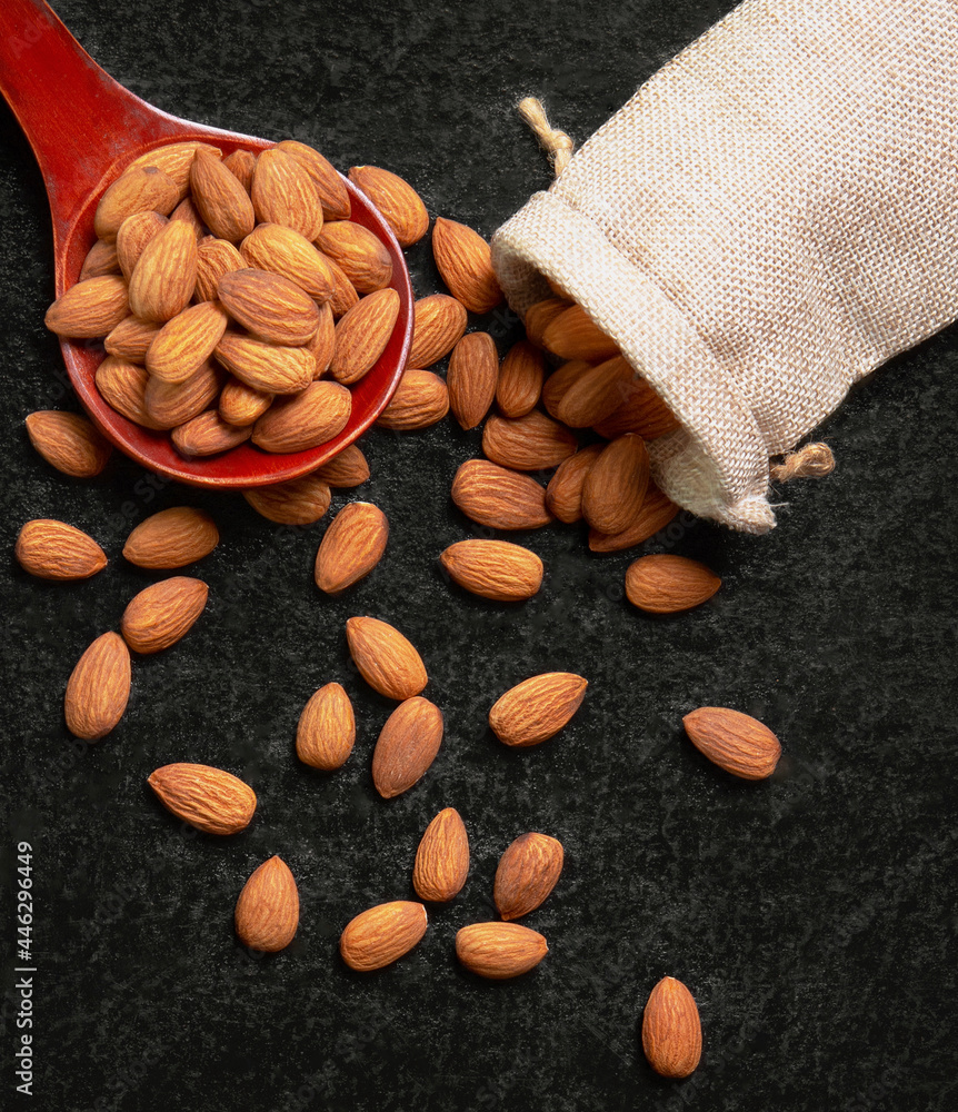 Almonds poured from wooden spoons and sacks on dark background. Almonds poured from wooden spoons and sacks on dark background.