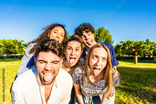 Group of silly young multiracial millennial friends making funny faces with tongue, open mouth, and squinting eyes posing for a portrait in city park. Live your life lightly while having fun in nature photo