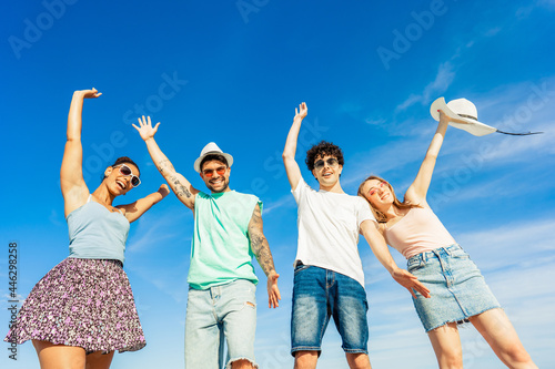 Young gen z happy multiracial friends group looking at camera for portrait in summer sea vacations. Bright vivid color photograph with blue sky. Diverse millennial people having fun at beach resort