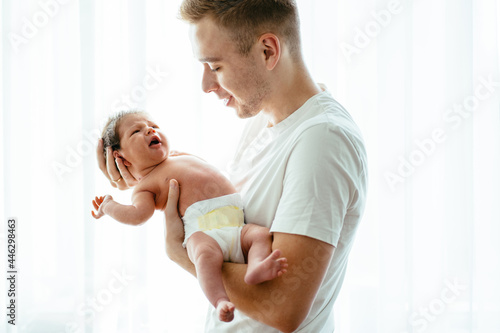 Parent love, tenderness concept. Portrait of father and son against light white background, caucasian white man holding his daughter on hands. Dad embracing his baby with love and care, smiling. © Iryna