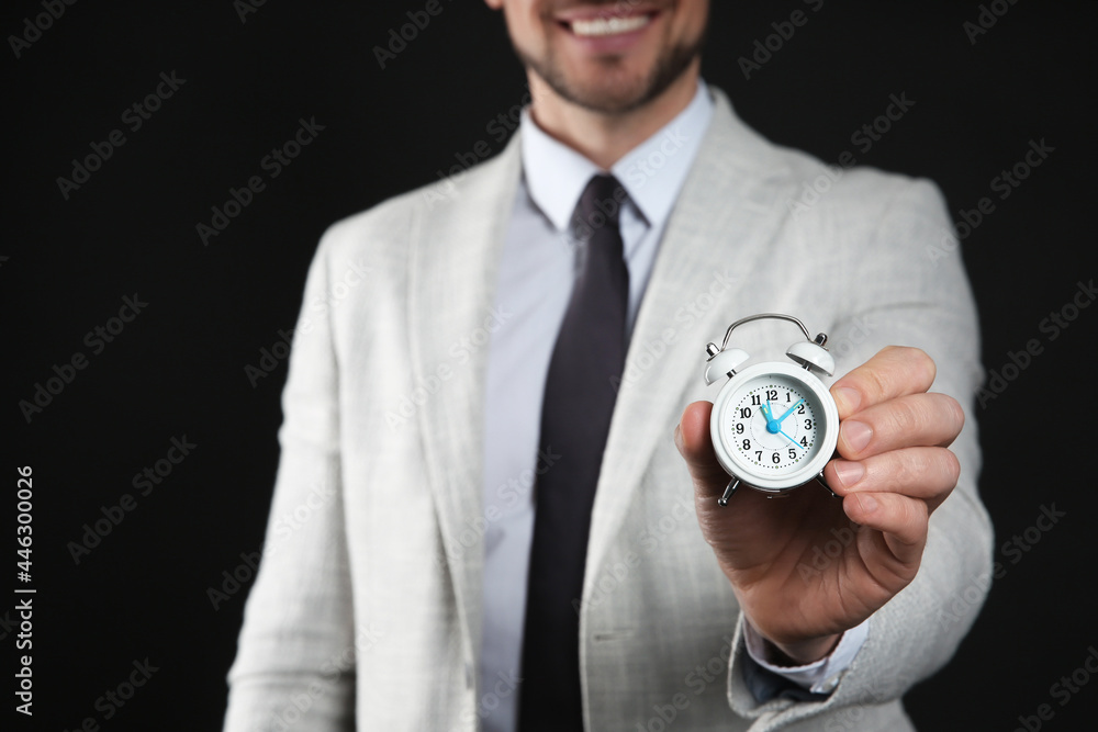 Happy businessman holding tiny alarm clock on black background, closeup. Time management Happy businessman holding tiny alarm clock on black background, closeup. Time management