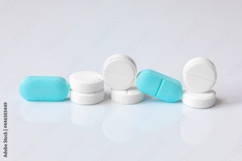 Round white pills and oval blue tablets on a light background for the design of a pharmacy store. Prescription drugs, pain relievers, or antibiotics. Pharmaceutical industry Round white pills and oval blue tablets on a light background for the design of a pharmacy store. Prescription drugs, pain relievers, or antibiotics. Pharmaceutical industry