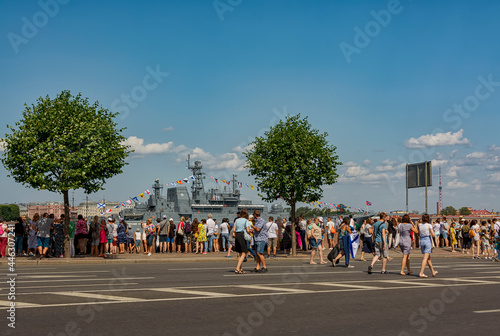 People walking along the embankment against the backdrop of the divorced Palace Bridge and warships. Rehearsal of the parade for the Day of the Russian Navy.