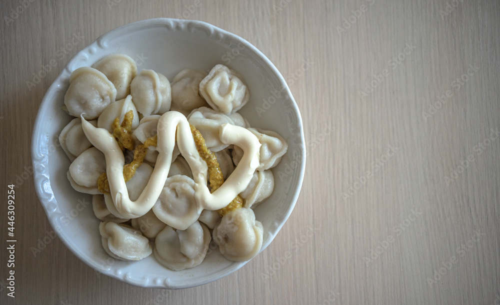 a white plate of dumplings poured with mayonnaise and mustard on a wooden kitchen table a white plate of dumplings poured with mayonnaise and mustard on a wooden kitchen table