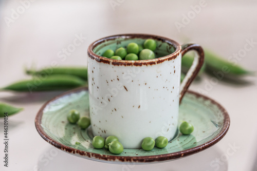 A cup full of fresh garden peas on green saucer with little peas with green pea pods in the background