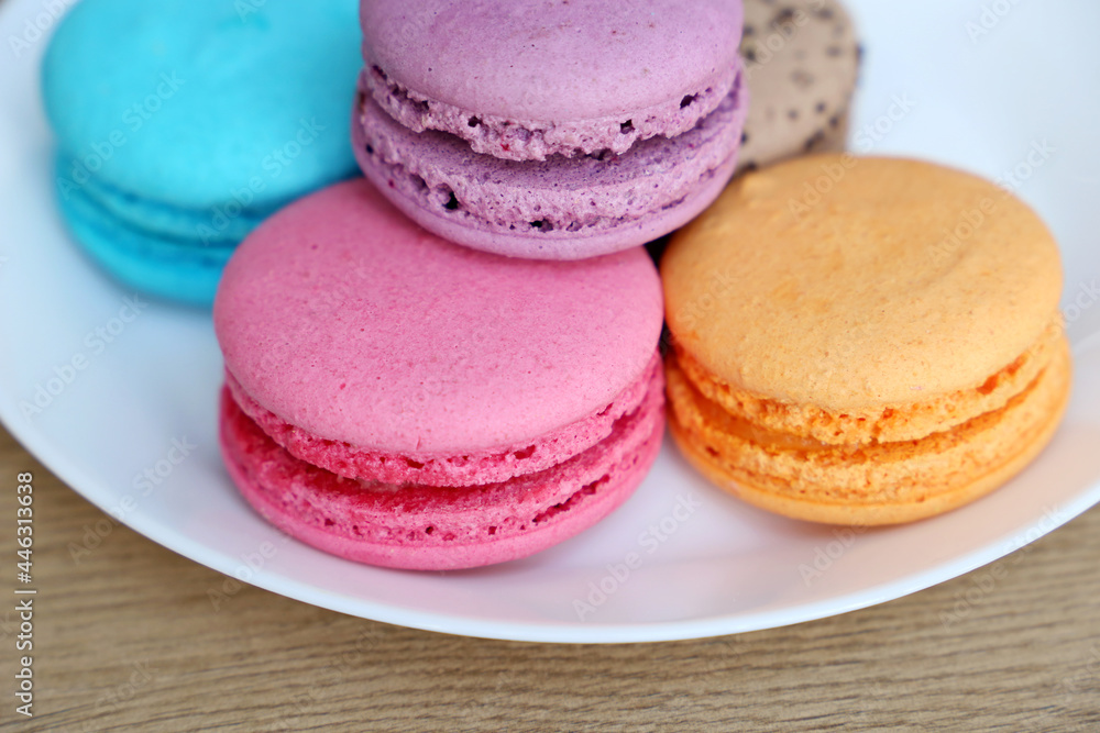 Macaroons in a white plate close up, colorful sweets. Strawberry, blueberry, vanilla and orange almond cookies with filling on a table Macaroons in a white plate close up, colorful sweets. Strawberry, blueberry, vanilla and orange almond cookies with filling on a table