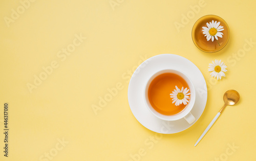 chamomile tea in a white cup with flowers and a vase on a yellow  background. Top view and copy space