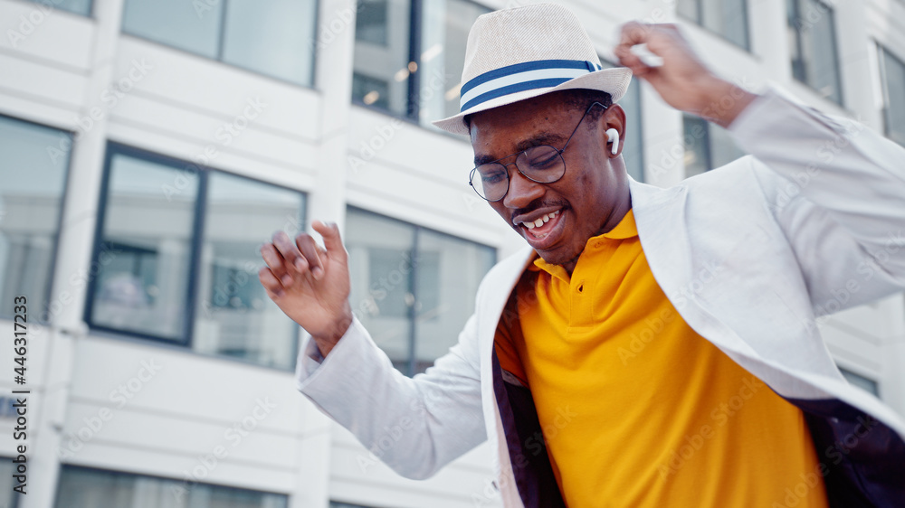 African American man in hat and wireless headphones listens to music and dances with joyful smile on megalopolis street African American man in hat and wireless headphones listens to music and dances with joyful smile on megalopolis street