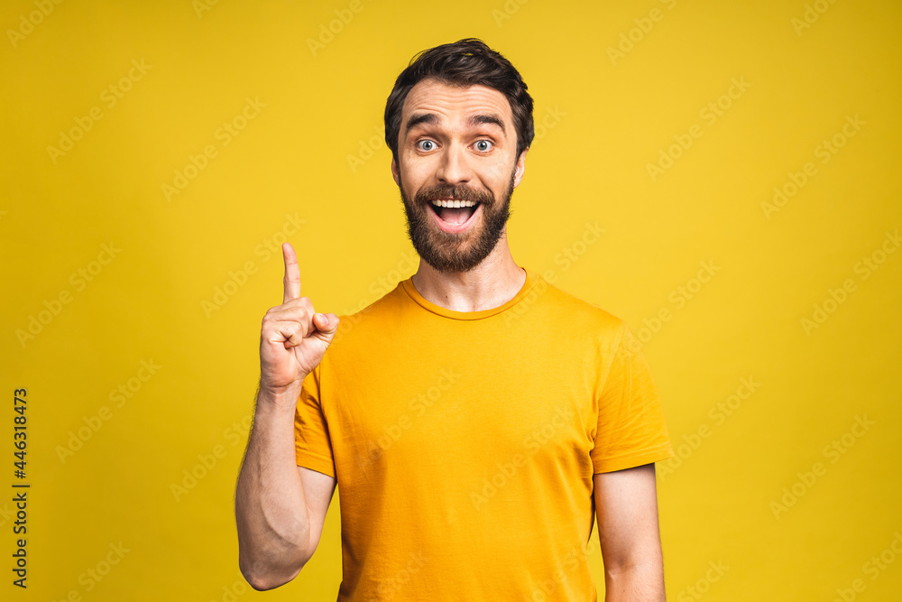 Look over there! Happy young bearded handsome man in casual pointing away up and smiling while standing isolated over yellow background. Look over there! Happy young bearded handsome man in casual pointing away up and smiling while standing isolated over yellow background.