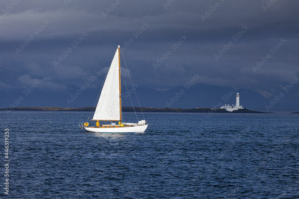 A yacht sailing towards the Eilean Musdile lighthouse on Lismore in the Inner Hebrides, Argyll and Bute, Scotland, UK