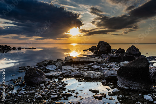 An image of a calm lake with a rocky shore at sunset. The clouds in the sky and the boulders on the beach provide a strong contrast to the warm setting sun at the end of a hot summer day. photo