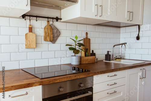 Kitchen brass utensils, chef accessories. Hanging kitchen with white tiles wall and wood tabletop.Green plant on kitchen background