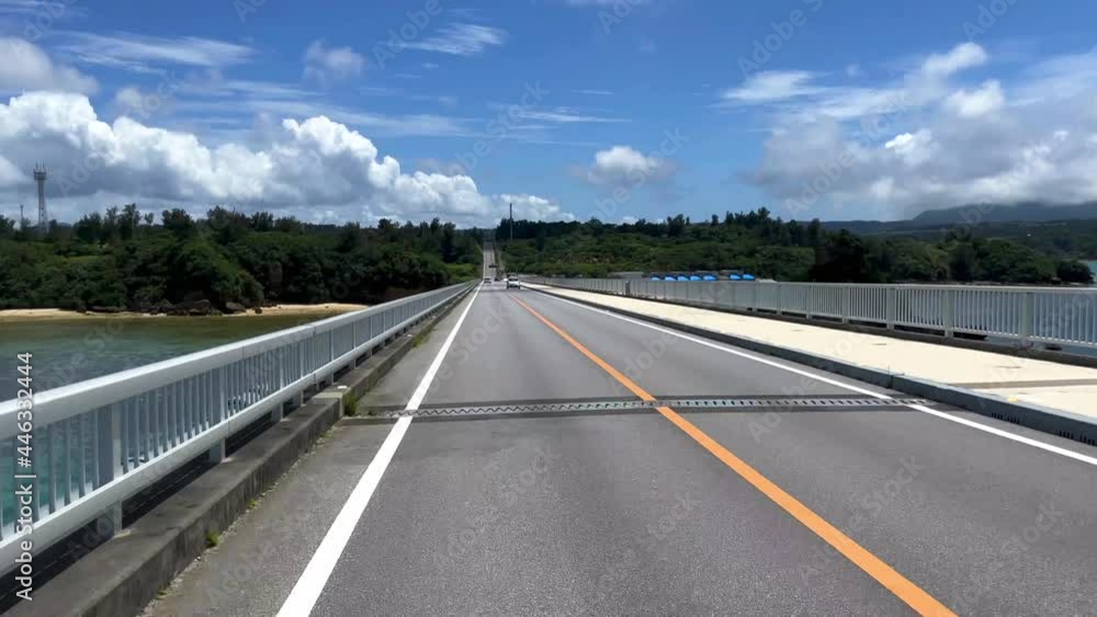 OKINAWA, JAPAN - JUNE 2021 : Driving at Kouri Island bridge. Wide camera, point of view (POV), seaside road driving shot. Blue sunny summer sky. Time lapse shot. OKINAWA, JAPAN - JUNE 2021 : Driving at Kouri Island bridge. Wide camera, point of view (POV), seaside road driving shot. Blue sunny summer sky. Time lapse shot.