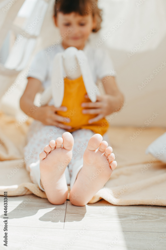 Fototapeta premium Child girl feet in teepee. Playing with fabric tilda bunny at home