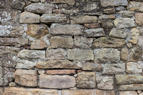 Gray rustic rocky wall built by many irregular stones.