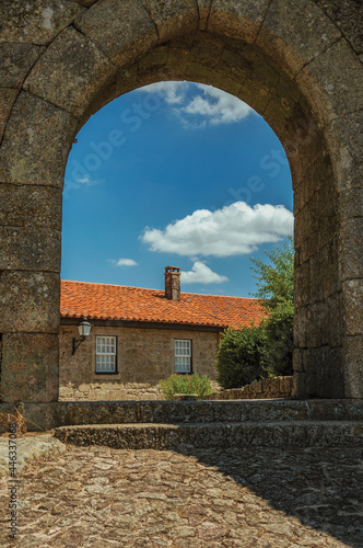 Stone old house and deserted alley seen through wall gate arch, in a sunny day at Sortelha. A well preserved medieval village in Portugal.