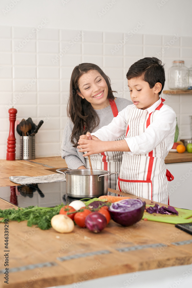 Mother teaches her son how to cook healthy food in the kitchen. Lifestyle with latin people. Child learning to cook.