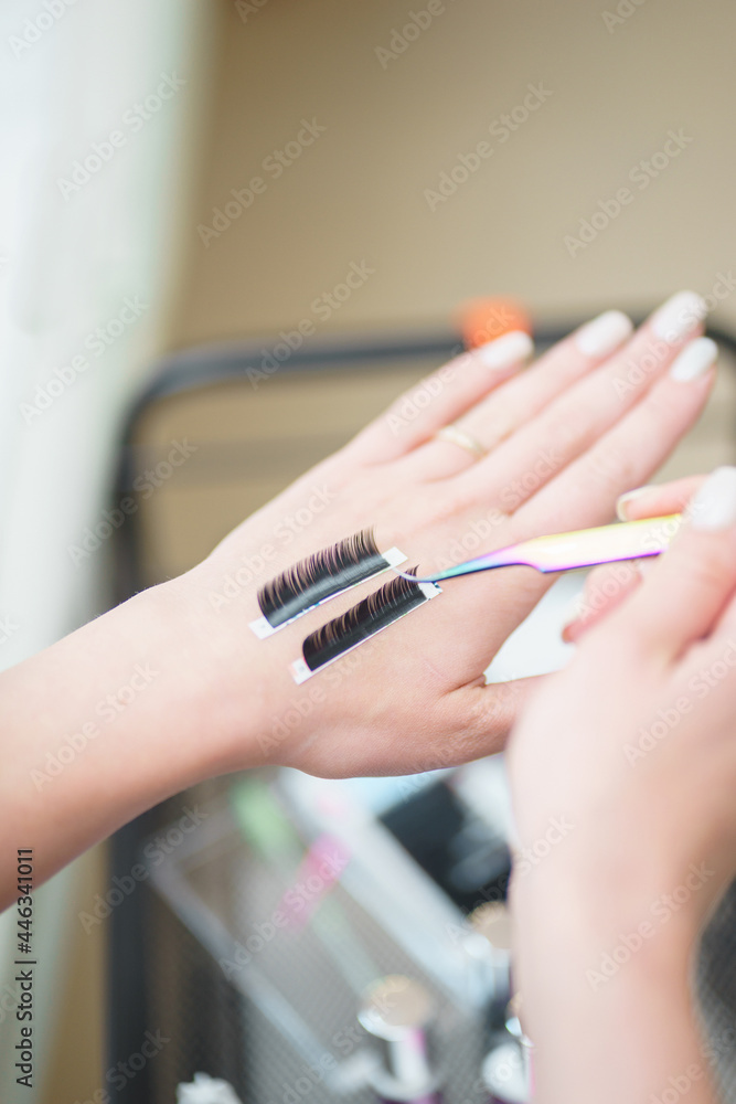 Aesthetic medicine, eyelash extension process: girl's hand with tools