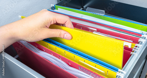 Hand pick yellow hanging file folder from open drawer. Administration clerk finding paperwork from office storage. Corporate information record, organized category and database management concept. photo