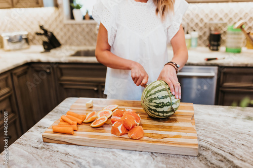 Woman slices watermelon, oranges, carrots, and ginger in her kitchen photo