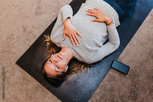 Woman meditates while laying on yoga mat in her home photo