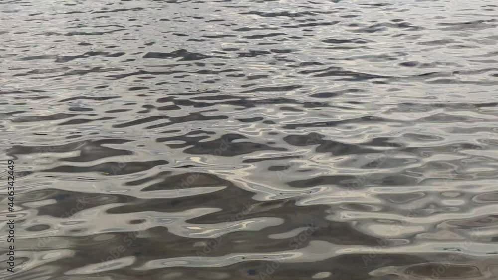 Water surface with fine ripples. Clean transparent water through which you can see the sandy bottom of the lake, on the surface of the water there are small constant waves that continuously fluctuate Water surface with fine ripples. Clean transparent water through which you can see the sandy bottom of the lake, on the surface of the water there are small constant waves that continuously fluctuate