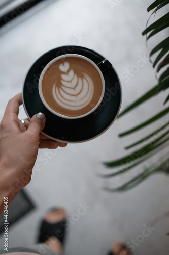 Woman s hand holding cappuccino coffee at coffee shop. Food drink photography concept. Tasty  atmospheric moody shot. Close up  top view