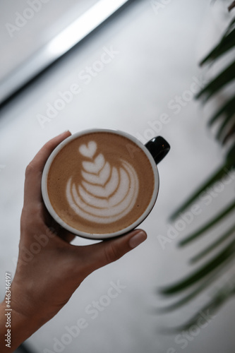 Woman's hand holding cappuccino coffee at coffee shop. Food drink photography concept. Tasty, atmospheric moody shot. Close up, top view